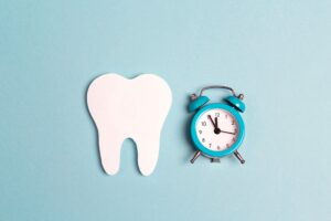 Wooden tooth next to a blue alarm clock on a pale blue background