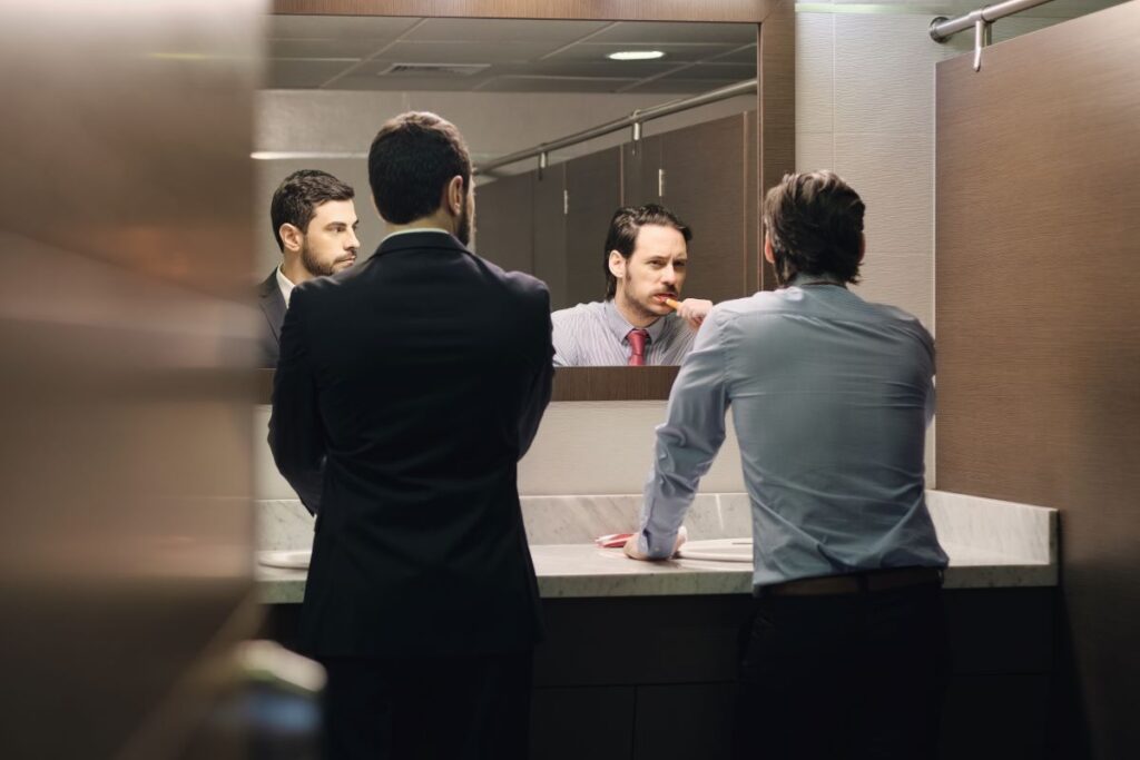 A man brushing his teeth in a public restroom.